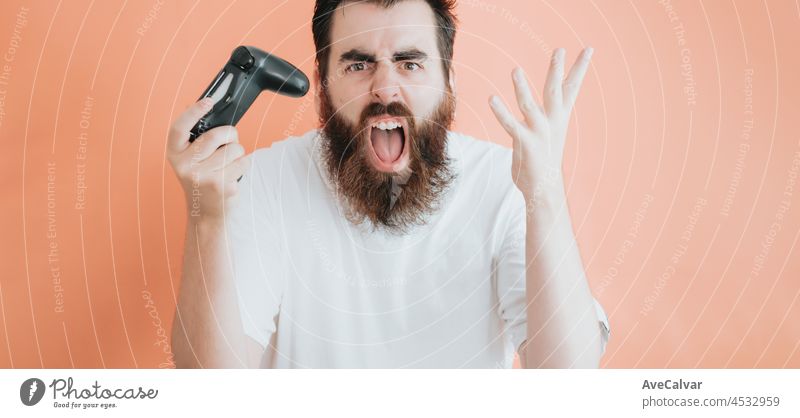 Young hipster bearded screaming while holding console pad, video games concept, copy space, soft orange removable background, minimal basic, ad concept deal, white shirt space