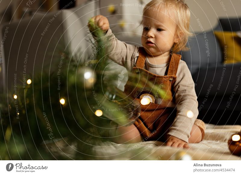 Lifestyle portrait of cute caucasian baby one year old playing with fir tree on floor at home. Merry Christmas xmas and happy new year 2022 christmas newborn
