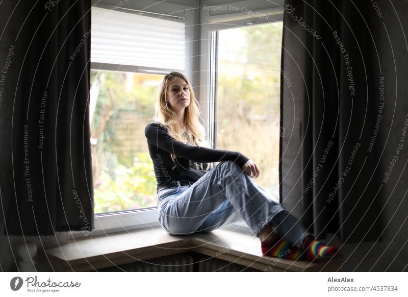 Young slim tall woman with long blonde hair sits in room in front of window Woman Young woman Large Blonde Long-haired pretty daintily Slim socks Striped socks