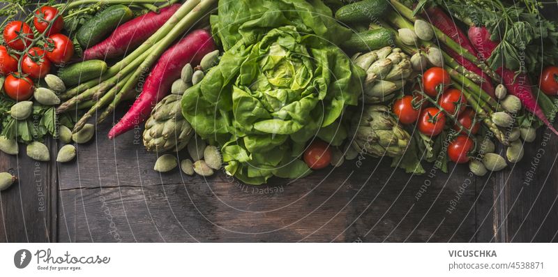 Various green and red vegetables on wooden kitchen table: lettuce, tomatoes, radish, artichoke, asparagus and cucumber. Healthy plastic free products on rustic background. Top view.