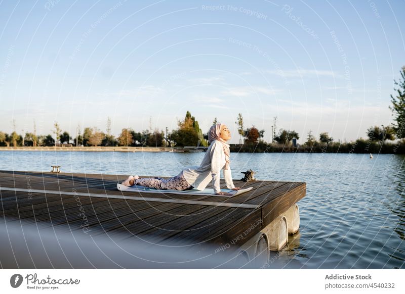 Arab woman doing Upward facing dog asana on embankment yoga upward facing dog urdhva mukha shvanasana waterfront river practice healthy lifestyle exercise