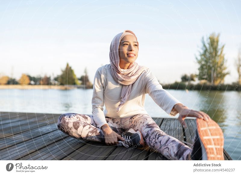 Sporty woman with a hijab warming up by doing stretch exercises outdoors in  the morning. Athletic