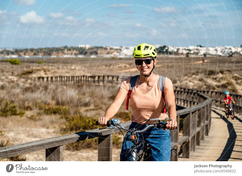 Mother riding a bicycle with her son on wooden walkways during summer day family bike ride nature helmet outdoor boy biker sport girl woman freedom relaxing