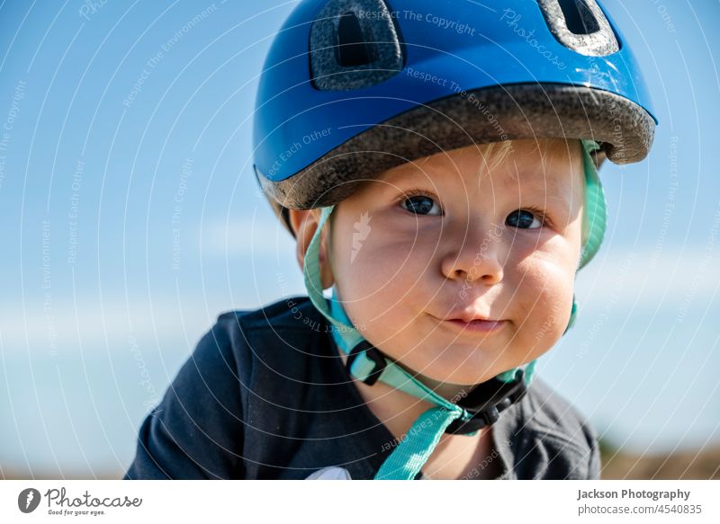 Portrait of a cute baby boy wearing blue bicycle helmet against blue sky bike people kid son family happy fun caucasian outdoors day childhood healthy active