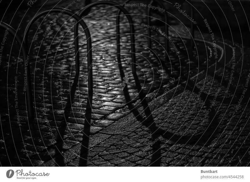 Bike racks and cobblestones in the shadow of the night Bicycle rack Deserted Metal Cobblestones Exterior shot Shadow Shadow play Night Light Old town Contrast