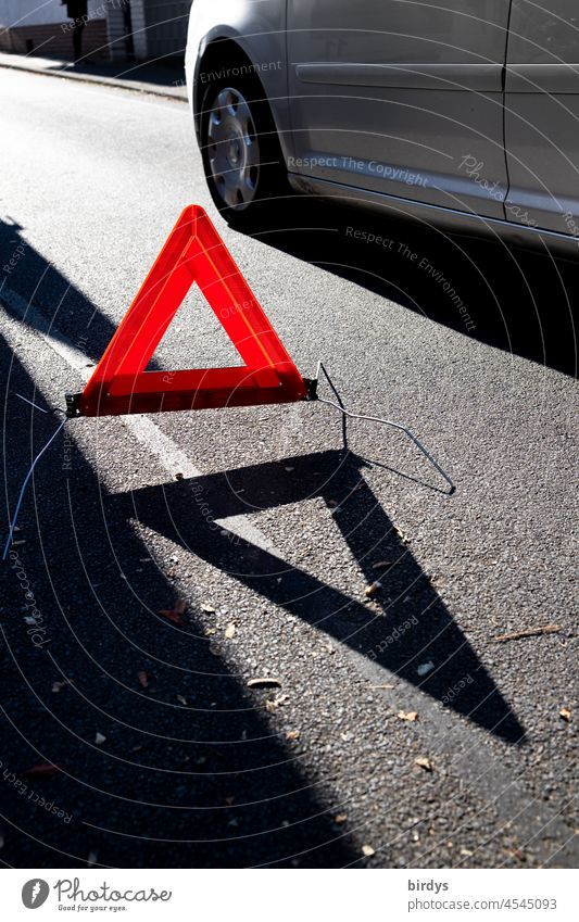 Bright red warning triangle with shadow cast on a broken down vehicle, accident scene. Car luminescent bright red Breakdown vehicle accident site Triangle Warn