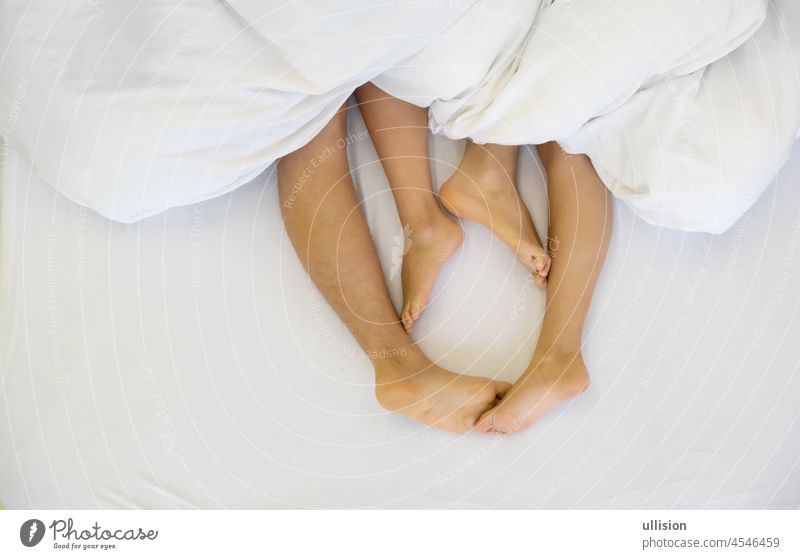 Close up of four feet, male and female, on bed - Loving couple having sex under white blanket in the bedroom - Concept of sensual and intimate moment, copy space
