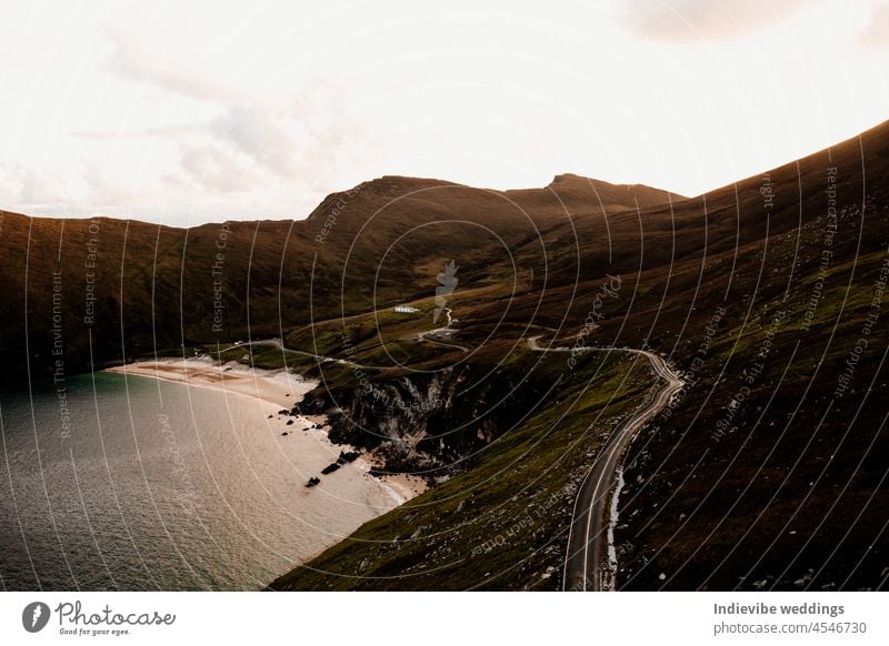 A beautiful sunset by the sea. A calm bay with mountains in the background. Empty road, drone photography. Bay Ocean Mountain Ireland Landscape drone view