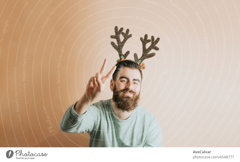 Young hipster beard man in stylish Christmas clothes having fun with a colorful removable background. New year concept. Fun and playful concept. Pointing copy space, using smart phone,