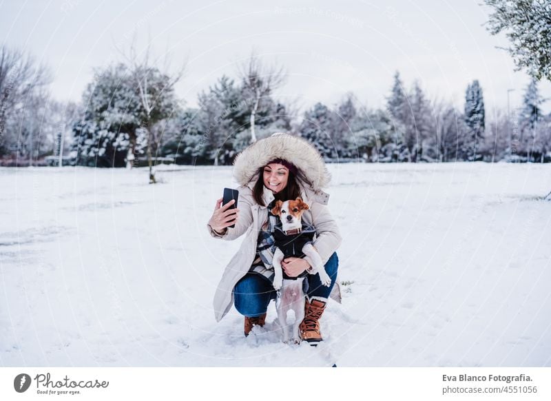 happy woman in snowy mountain taking picture with mobile phone with cute jack russell dog. winter season. Fun in the snow selfie tech camera internet connection