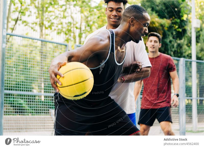 Group of friends jumping and tossing ball up men basketball play player game street sport positive man cheerful diverse throw multiracial happy sun joy together