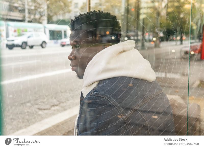 Thoughtful black male sitting on bus stop on street man pensive thoughtful wait city road urban style african american serious alone appearance guy town station