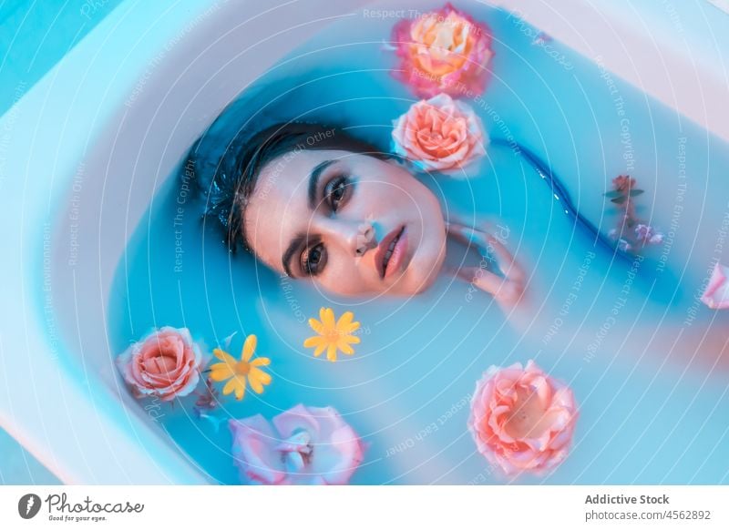 Young woman in bathtub with flowers in blue light wet hair sensual lying melancholy model seductive tender allure delicate tranquil relax gentle serene portrait