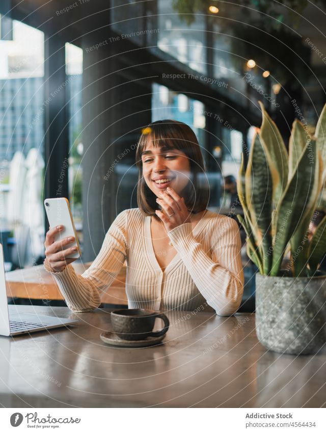 Cheerful woman with cup of coffee using mobile phone laptop browsing device connection remote businesswoman freelance drink internet communicate gadget