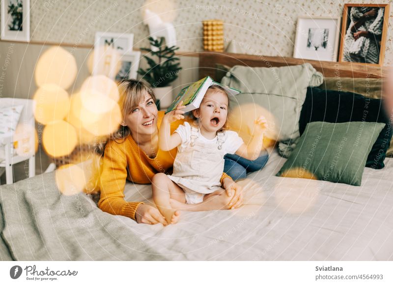 Mom and daughter are reading a book and smiling, sitting at home on the bed. New Year, Christmas, family, time together mom christmas christmas lights year new