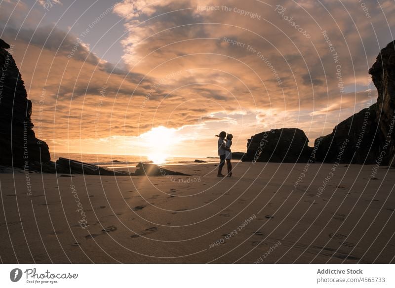 Couple standing on beach in evening couple silhouette embrace sundown sunset hug together twilight shore picturesque walk beach of the cathedrals galicia spain