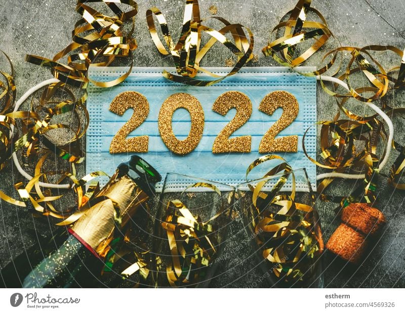 New Years Eve celebration concept background.Medical mask with the numbers 2022 and Champagne bottle with glasses .Covid-19 New Year concept on gray background