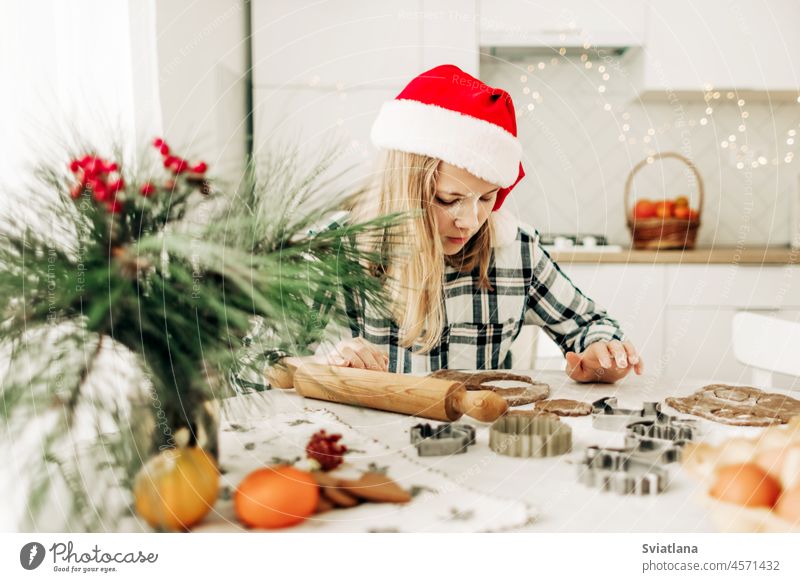 A girl in a red Christmas hat is making gingerbread dough in the kitchen. Christmas tradition, Christmas atmosphere, preparation for the holiday child christmas