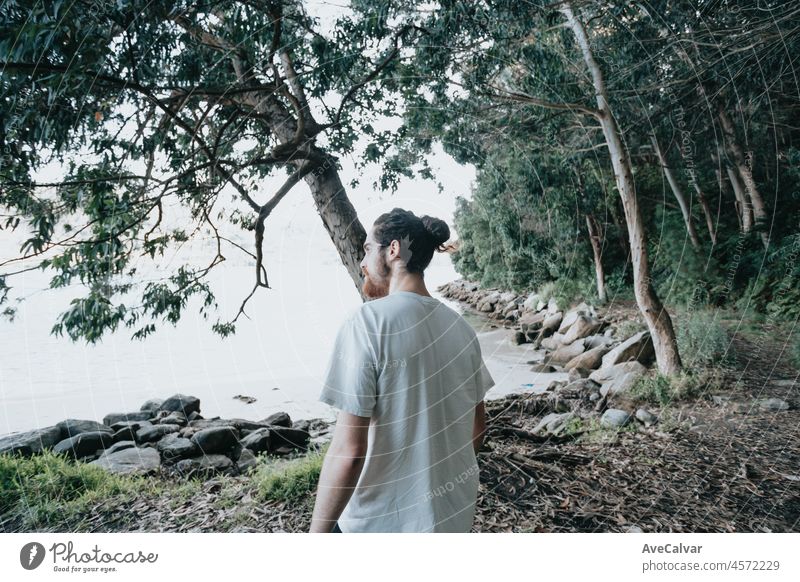 A young modern man walks on the path of rocks on the shore and looks at the evening sea.Young hipster girl doing some hiking on the shore, traveling and low budget travel concepts, copy space