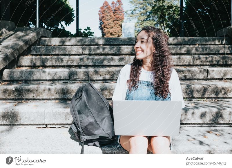 Focused young happy African american student sitting on stairs at university using a laptop to do research about university works and paper. Education.Making notes, online lectures, gaining knowledge