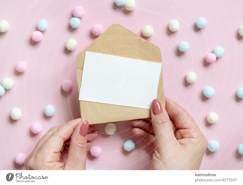 Hands with blank card  and envelope near pastel pom-poms on pink top view WEDDING hands pompom mockup girlish paper valentine spring mothers day above