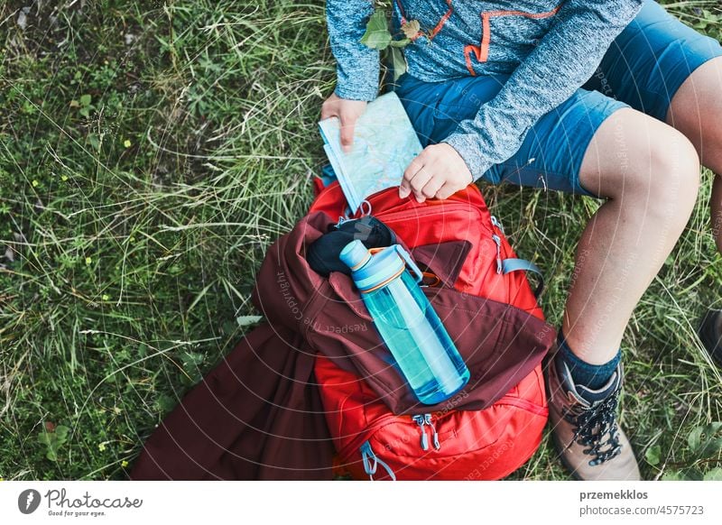 Woman with backpack having break during trip in mountains taking map out sitting on grass summer active woman adventure activity fun travel trekking vacation