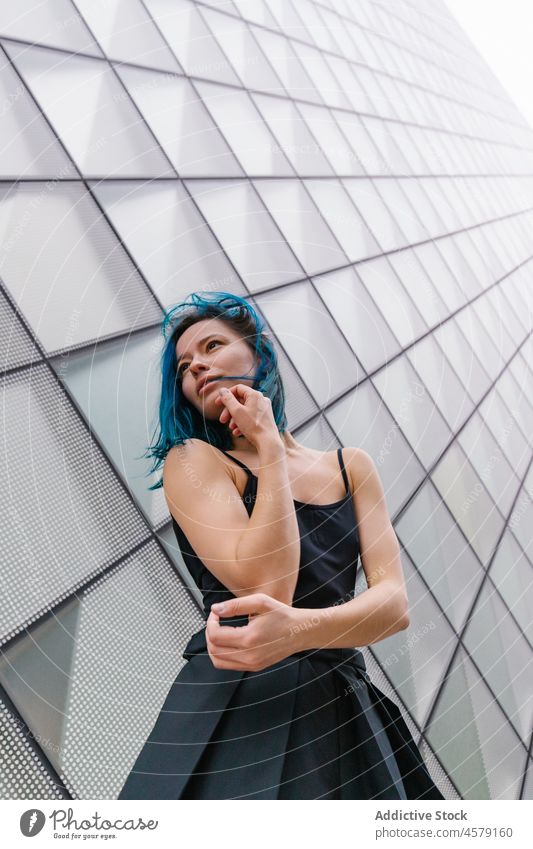 Female with blue hair standing near wall of modern building woman appearance contemporary portrait urban skyscraper trendy street city female outfit style