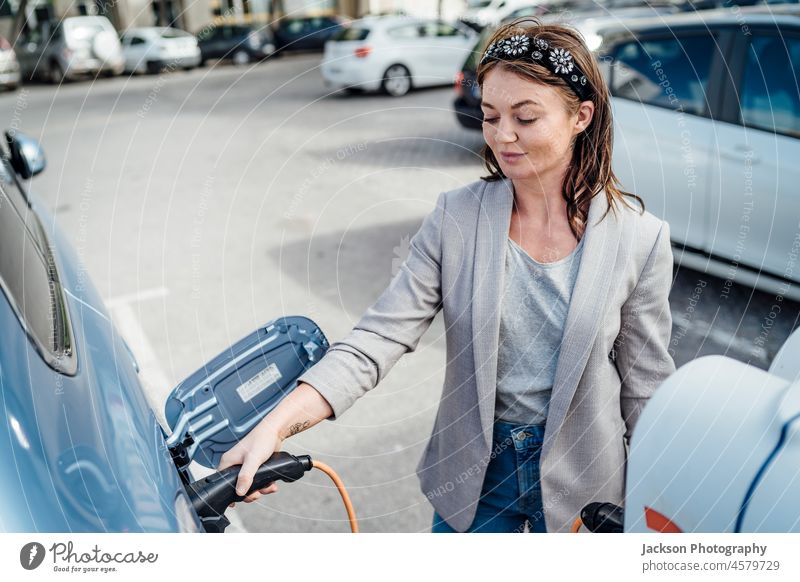 An elegant woman charging an electric car in urban settings charge charging station caucasian renewable energy holding attractive business woman outdoors plug