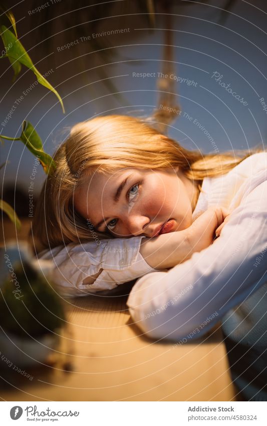 Discontent young girl leaning head on hand sitting at desk woman lamp illuminate touch chin blouse white home problem evening concern upset dissatisfied