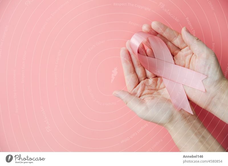 Female hands holding pink ribbon over pink background, breast