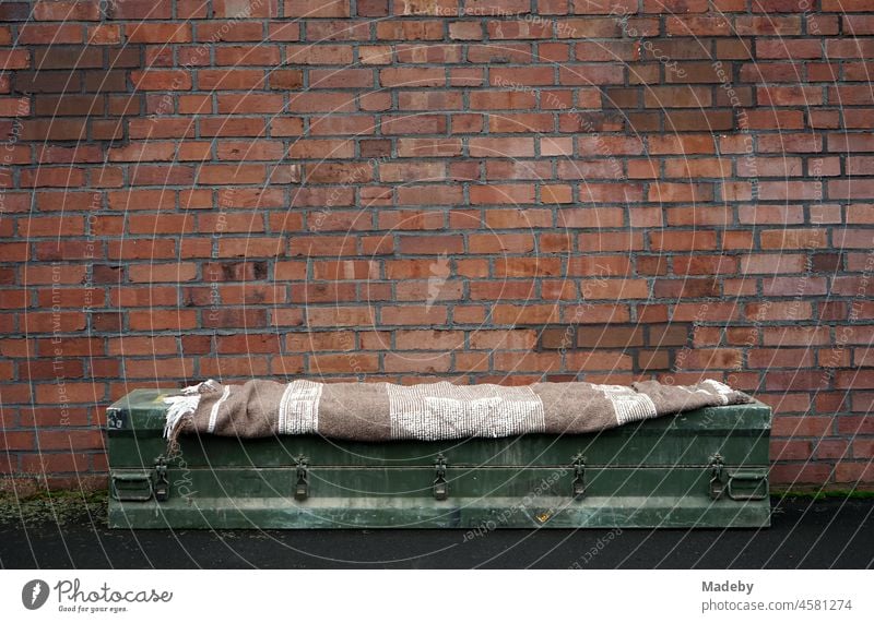 Solid green old rifle box with striped brown woollen blanket as a bench in front of a reddish brown old factory wall on a former factory site in the Margaretenhütte district of Giessen on the river Lahn in the German state of Hesse