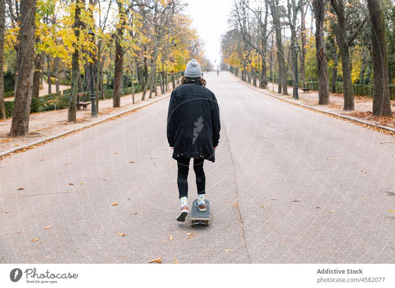 Anonymous female skater riding skateboard in autumn park woman ride hobby defocused happy road asphalt casual nature energy activity longboard positive active