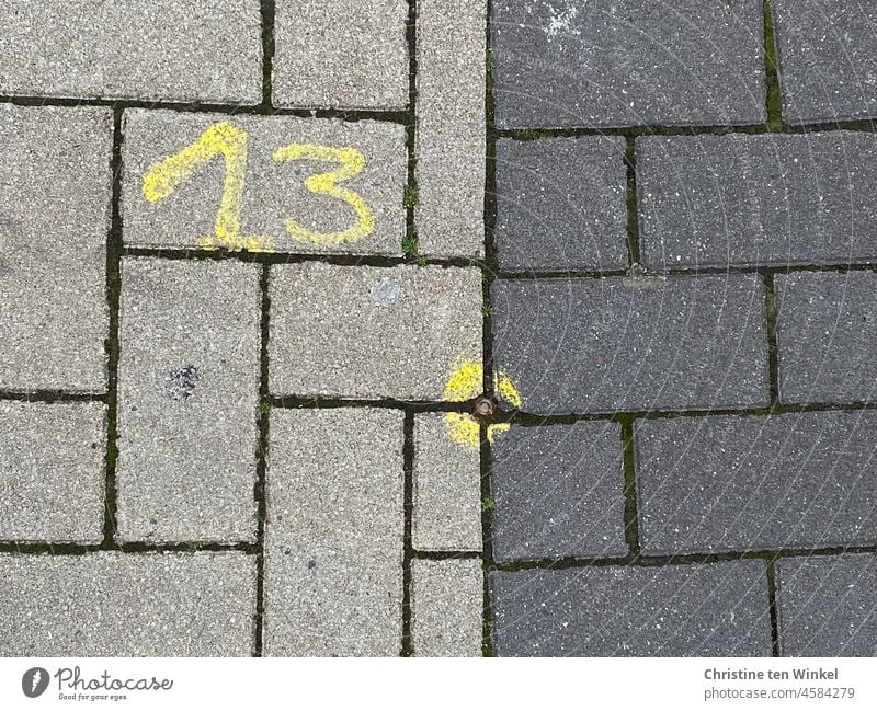 A yellow 13 and a yellow mark on light gray and dark gray pavers number Digits and numbers thirteen Circle Point Yellow Paving stone Dark gray off Pavement