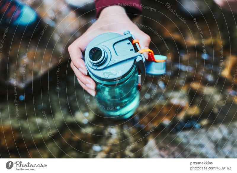 Woman taking pure water to bottle from mountain stream during trekking in mountains adventure trip travel hiking thirsty vacation journey crouching summer