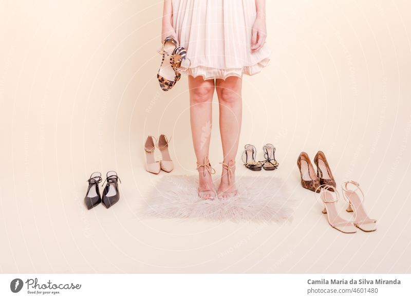 Stylish girl standing in pink pleated dress surrounded by a variety of shoes. She is dressed in a pink pleated skirt, on her feet blue shoes. Shoes assortment