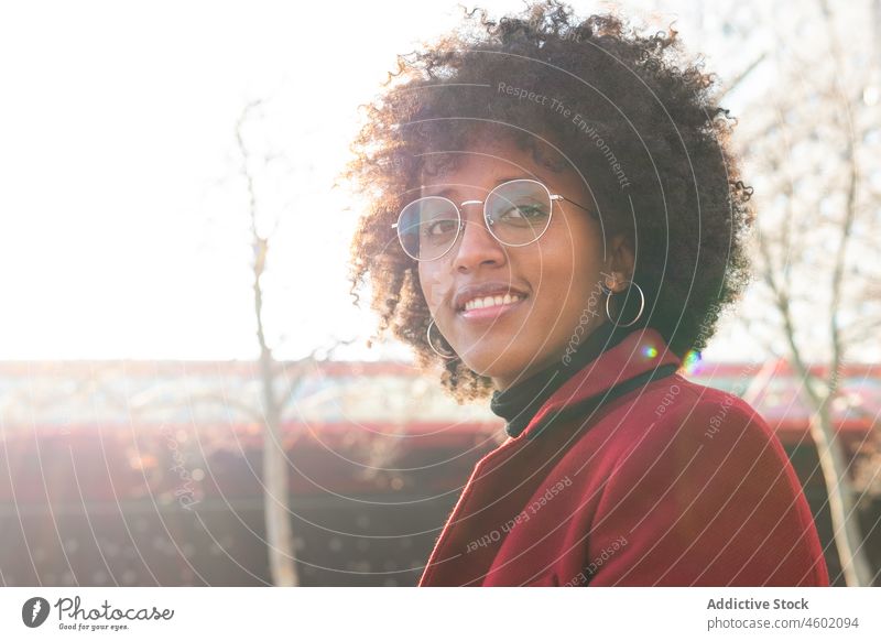 Smiling African American woman in crimson coat and eyeglasses afro hairstyle positive curly hair casual portrait cheerful sunlight smile happy charming optimist