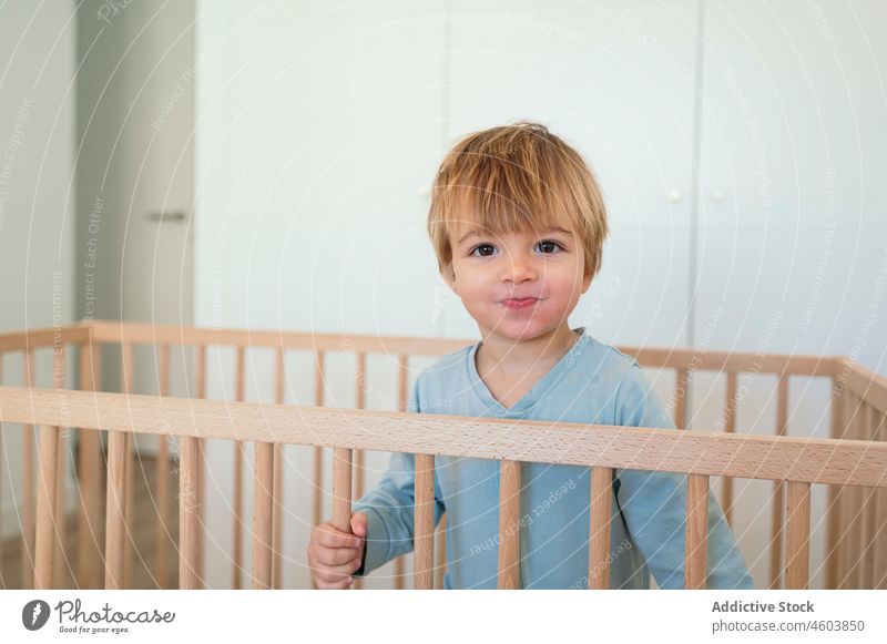 Cute boy standing in crib toddler child childhood bedroom cot awake domestic home bed time light cute curious wardrobe adorable little wooden innocent casual