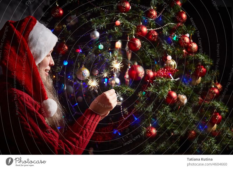 woman in a Santa hat with lighted sparklers on the background of a New Year or Christmas tree decorated with red ball. celebrate new year christmas party happy