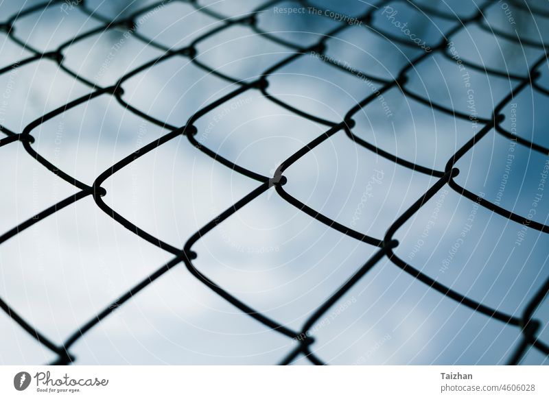 Dramaic blue sky with white clouds through a metal grid chain fence . low angle view background crime freedom prison protection safety security steel boundary