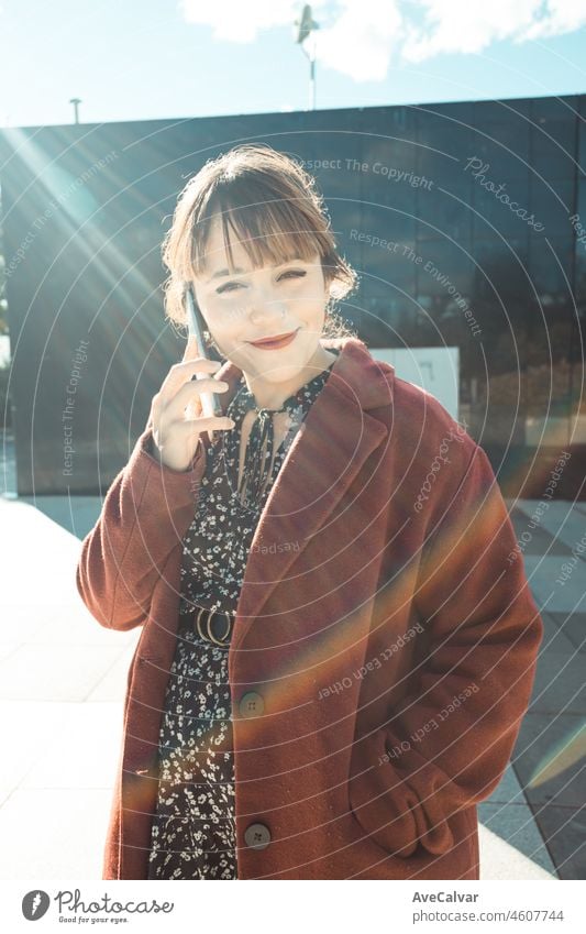 Young beautiful red head woman outside office velvet coat using mobile phone and looking happy while standing and negotiating on the phone, young woman business concept. Bright future concept