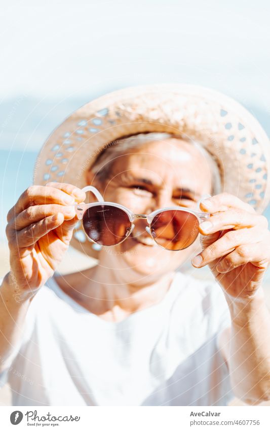 Happy senior woman smiling while holding the sunglasses. Retirement resting, new healthy habits, traveling and doing activities. Smiling and having fun outdoors