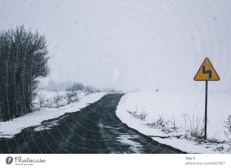 a sign warns of a bend in a wintry little road. Country road Winter Curve poliska Poland Snow Asphalt Road sign Street Exterior shot Traffic infrastructure