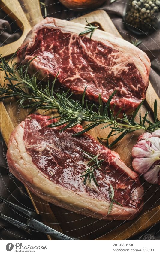 Close up of two raw marbled steaks with fresh rosemary and garlic on rustic cutting board. Top view close up top view beef beefsteak cooking entrecote fillet