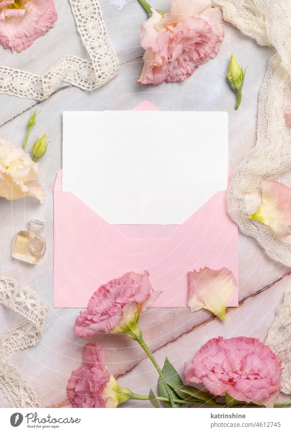 Pink flowers and a blank card with envelope laying on a marble table mockup greeting birthday Wedding roses top view ribbons flat lay retro message perfume