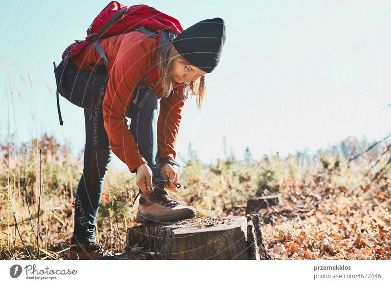 Woman tying laces on hiking boots while hike on vacation trip. Hiker with backpack taking break during walking adventure travel exploring journey wanderlust