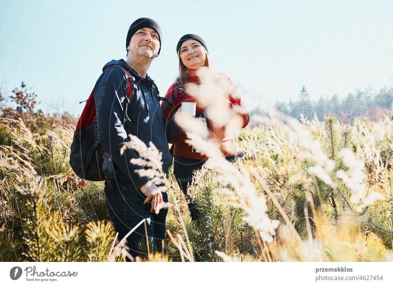Couple enjoying nature while vacation trip. Hikers with backpacks looking at mountains view. People standing in tall grass on path to mountains on sunny day