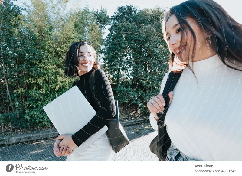 Couple of young woman student Of College Walking Through the campus. They walks trough university campus and laughing after meeting again at the university. Study together and learning concept. Trendy