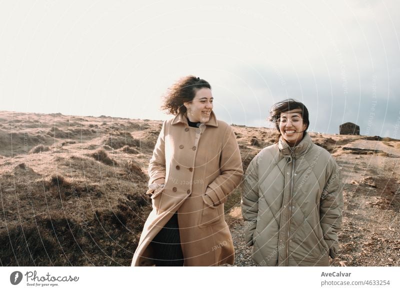 Young woman Two Friends on the meadow Laughing and Walking during a colorful sunset. Copy space, Film concept. Friendship and travel together road trip style image. Normal people