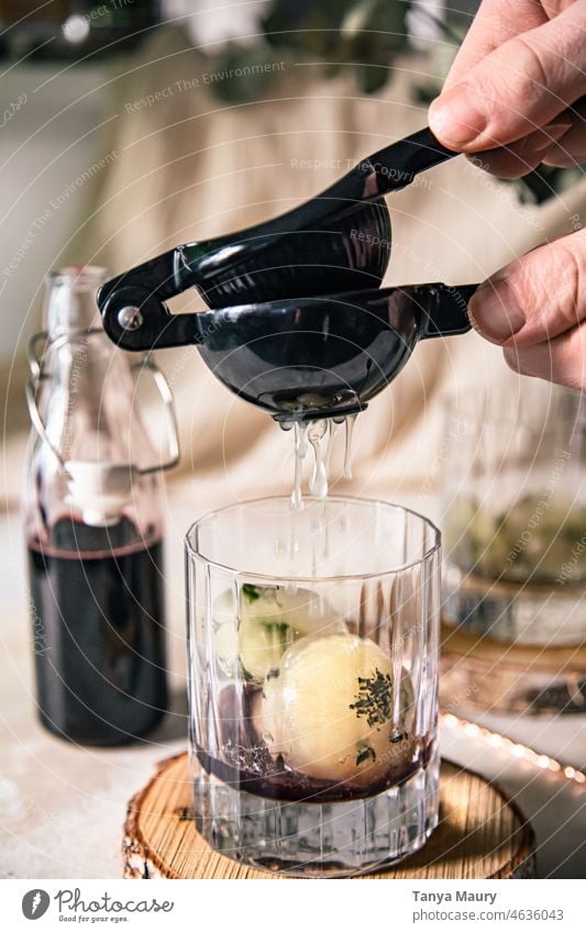 hand pressing a lemon in a cocktail made with edelberry syrup and herbal ice cubes glass kitchen rosemary liquor homemade food healthy freshness green