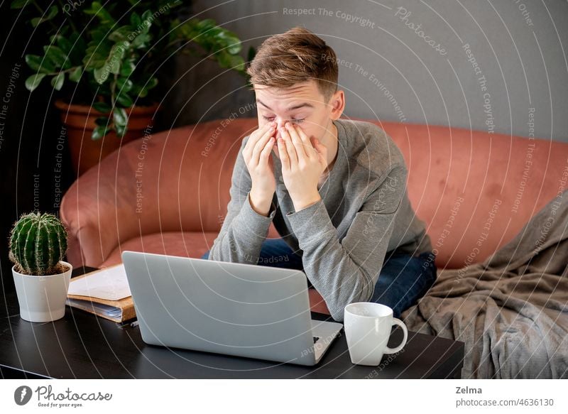 Young man sitting at window and working on laptop. Bearded man sitting at  desktop with smartphone in his hands. Online education. Stock Photo